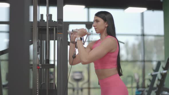 A Hispanic Brunette Woman in a Pink Suit Pulls a Rope in a Crossover with Her Hands to Train Her