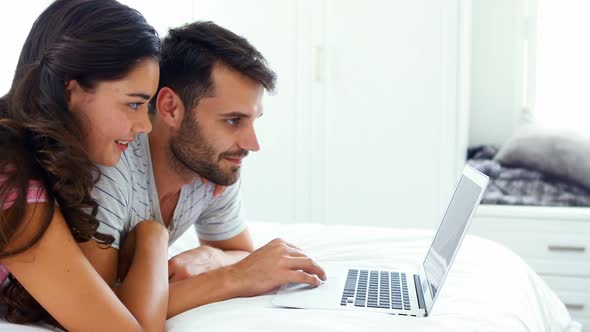 Couple interacting with each other while using laptop on bed