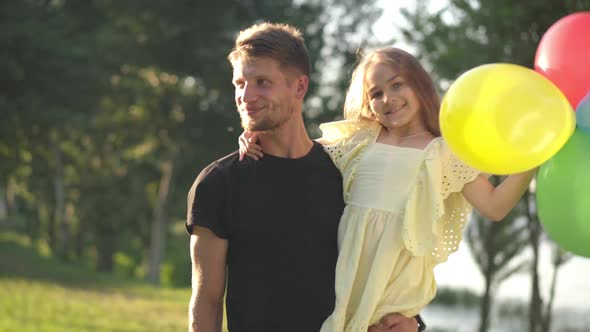 Happy Handsome Young Father Holding Daughter with Multicolored Balloons Talking Smiling