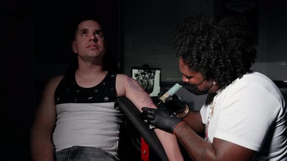 Professional African American Tattoo Artist Makes a Tattoo on Client Arm