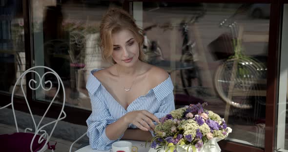 Young Girl Sitting In A Cafe And Admires A Bouquet Of Flowers