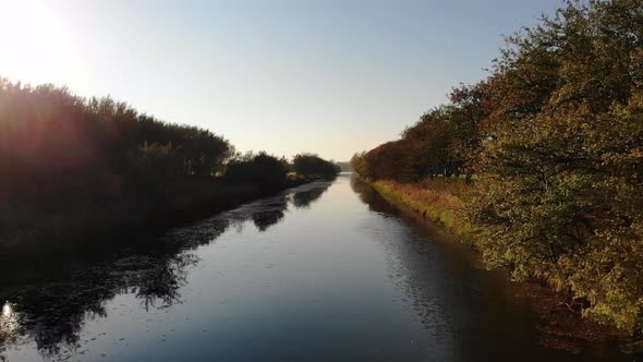 Aerial view of beautiful river with rows of trees in autumn colours, moving towards the sun in Odher