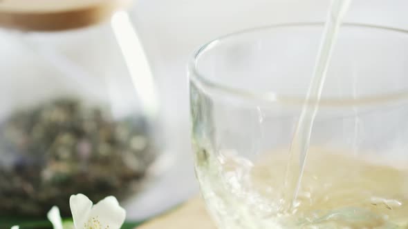 Freshly Brewed Green Tea Is Poured Into Glass Cup. Close Up. In Background Is Transparent Green