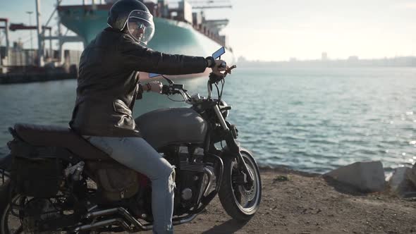 Motorcyclist Sits on an Old Caferacer Motorcycle Harbor Background