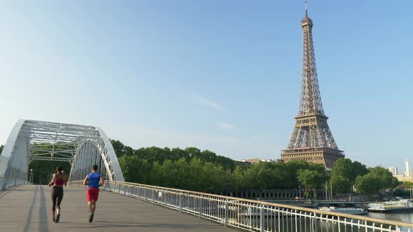 A man woman couple running across a bridge with the Eiffel Tower