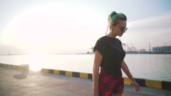 Young Stylish Funky Girl with Green Hair Riding Roller Skates and Dancing Near Sea Port During