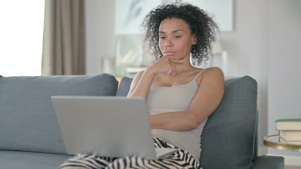 Pensive African Woman Thinking and Working on Laptop at Home