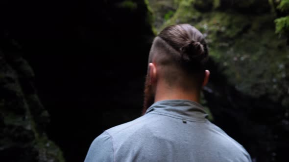 Back view of young man slowly walking further into a shadowy ravine