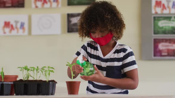 Boy wearing face mask spraying water in plant pot