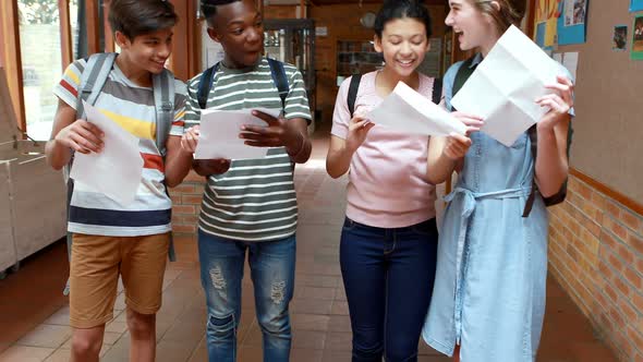 Happy classmates looking at grade cards in corridor