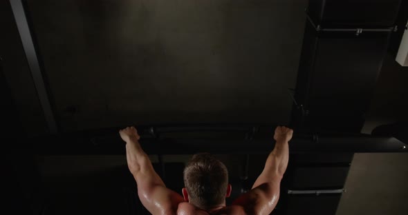 A man with beautiful muscles on his back, in the gym, pulls himself up on a horizontal bar