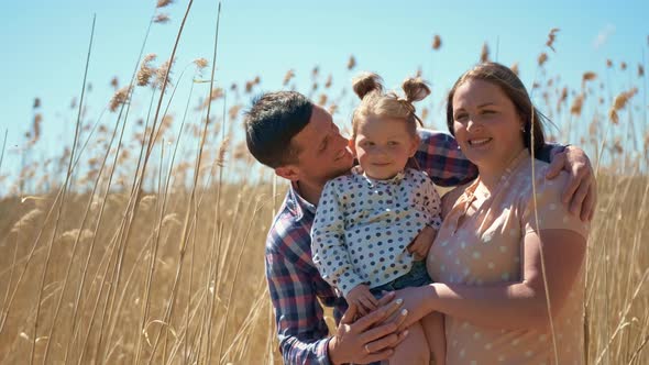 Happy Young Couple with a Little Girl in Their Arms on Nature on the Background of Reeds