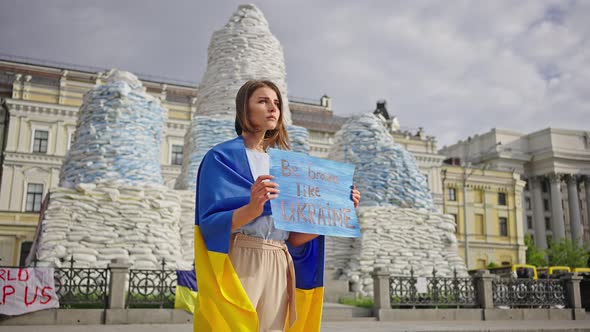 Ukrainian Woman with Poster Stands Against Covered Monuments