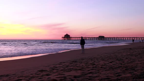 A panning shot of a man enjoying the beach on vacation during a gorgeous yellow, orange, pink and bl