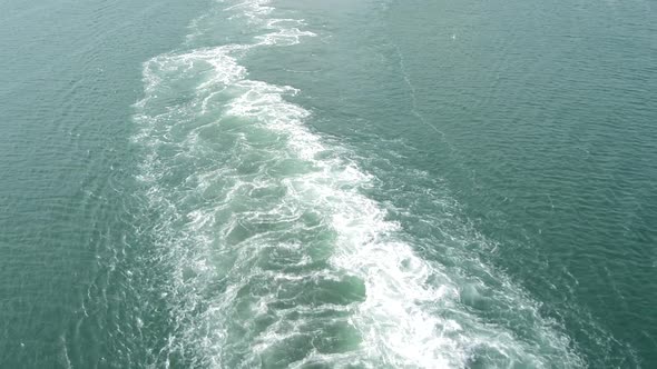 A foaming, bubbling trail on the blue surface of the water from the movement of a large ship at sea