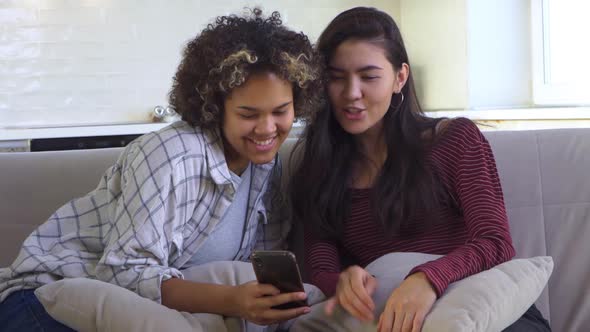 Two Girlfriends Looking at a Smartphone While Sitting on the Couch