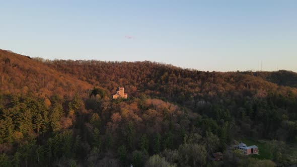 Autumn view of church tucked into forest on the side of a mountain with sunshine and blue sky.