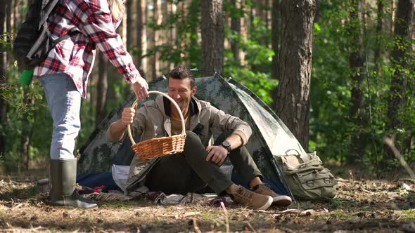 Positive Handsome Caucasian Man Sitting at Camp Tent Greeting Young Woman Returning From Forest with