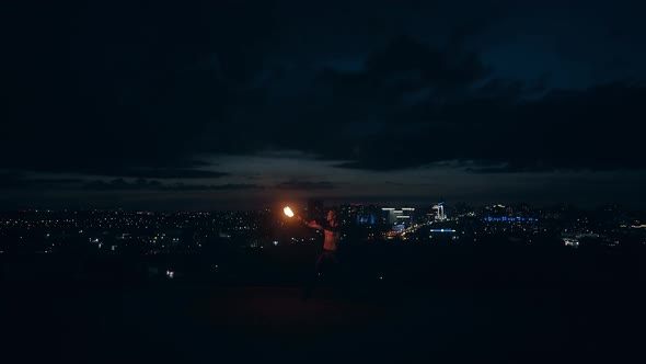 Young Blond Male Does Tricks with Fire, Breaths Fire at Night with City Skyline in the Background