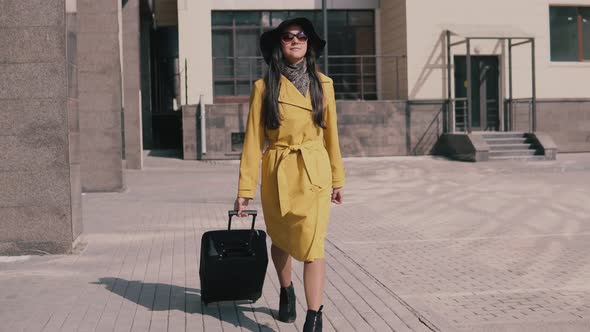 Stylish Young Girl in a Yellow Raincoat Hat and Glasses Comes with Luggage