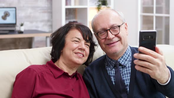 Cheerful Old Couple Sitting on Sofa Taking a Selfie