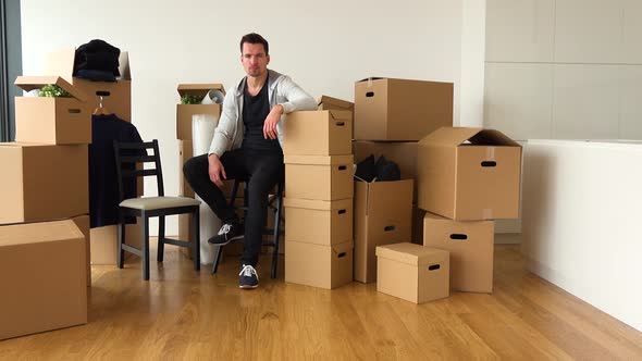 A Moving Man Sits on a Chair and Looks Seriously at the Camera in an Empty Apartment