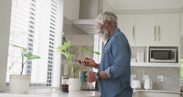 Video of african american senior man drinking coffee and using smartphone