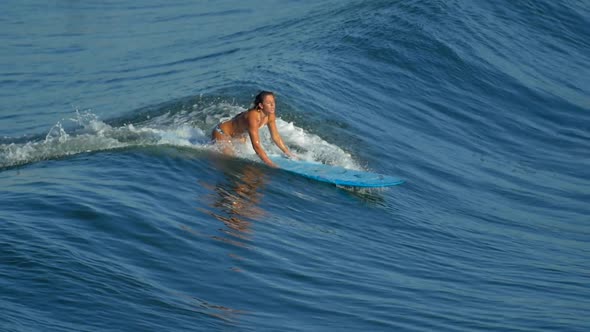 A young woman surfing in a bikini on a longboard surfboard.