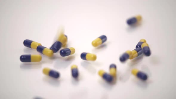 Slow Motion Macro of Blue and Yellow Pills Dropped onto White Background