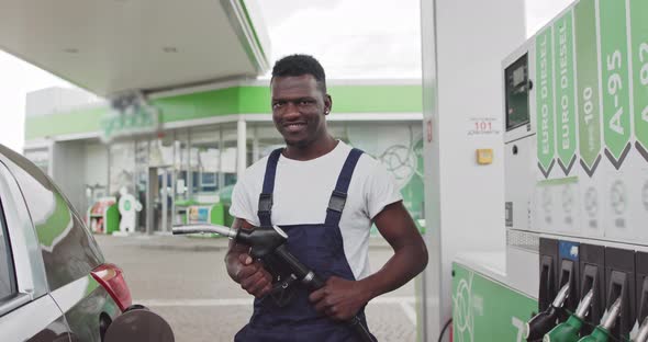 Black African Gas Station Worker Holding a Pistol to Refuel a Car