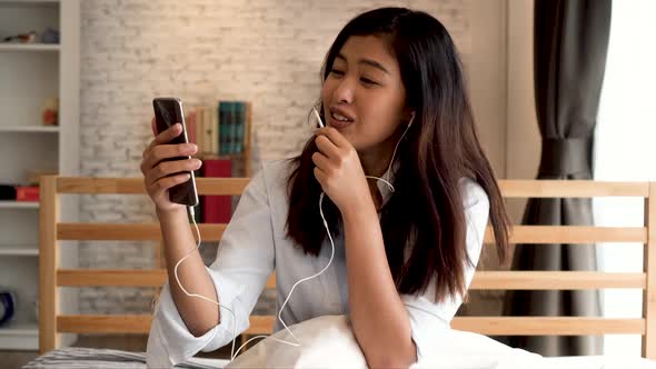 Portrait of Happy Young Asian Girl in Casual Clothing Lying Down on Bed While Making a Video Call