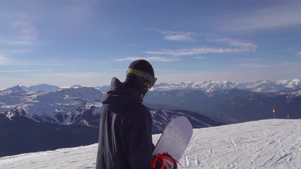 A young man snowboarder walking with his board on a scenic snow covered mountain top.