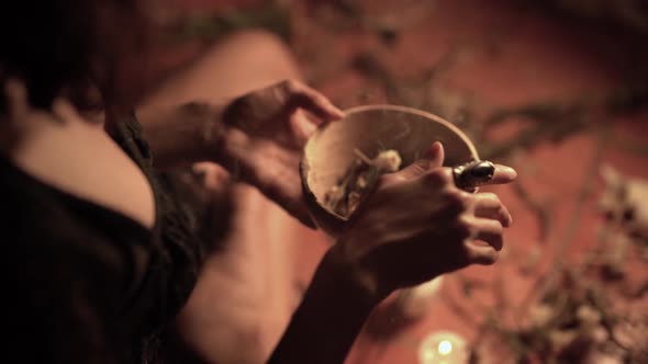 Crop witch conjuring over bowl with herbs