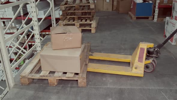 Factory Man Is Loading Cardboard Boxes on a Hand Pallet Truck in Warehouse