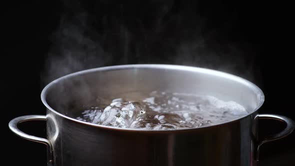 Pot of Boiling Water Over Black Background. Bubbles of Boiling Water. Slow Motion Shot