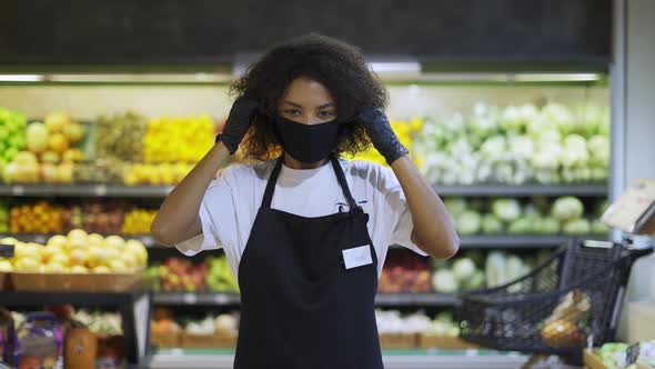 Portrait of Happy African American Female Worker Standing in Supermarket Putting on Protection Mask