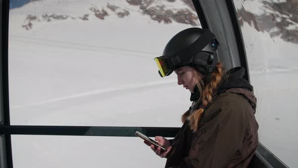 Woman With Red Plaits And Skiwear Texting On Phone In Cable Car