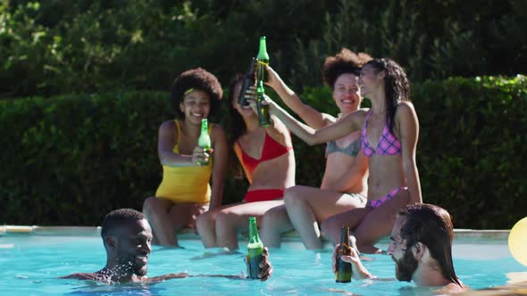 Diverse group of female friends eating watermelon sitting at the poolside drinking beer