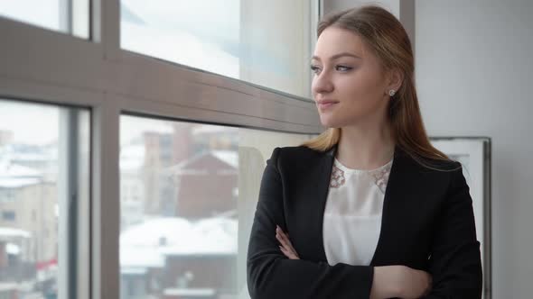 Serious Businesswoman in Black Suit Looking to Window in Modern Office