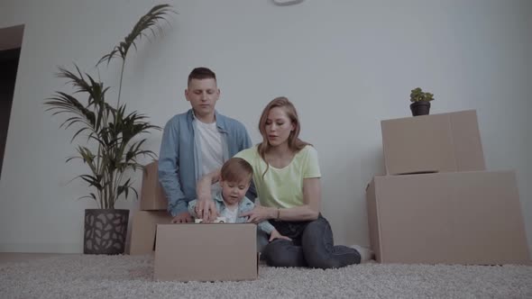 Image of Happy Couple with Children Sitting on Floor Among Cardboard Boxes