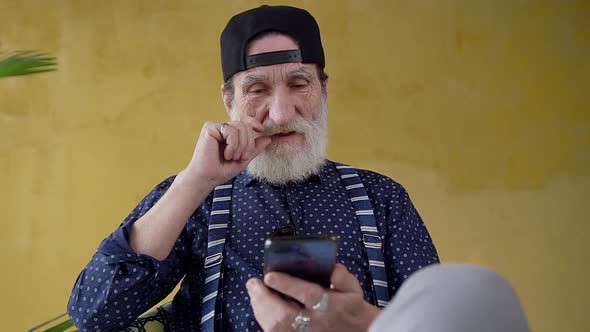 Bearded Stylish Man in Youthful Cap which Using His Smartphone
