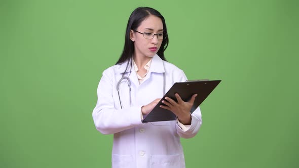 Young Beautiful Asian Woman Doctor Thinking While Holding Clipboard