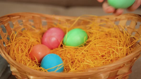 A Child's Hand Puts Easter Colored Eggs in a Yellow Wicker Basket