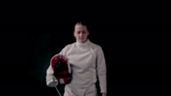 Fencing Training - Young Woman Walking Out From the Dark and Putting on a Protective Helmet - Gets