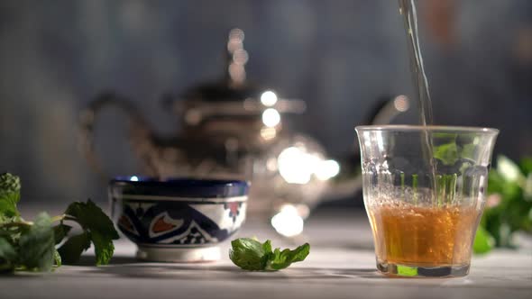 Cinemagraph of tea midway pouring into a glass with Moroccan tea set and mint.