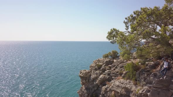 Aerial View of Young Man Traveler on Rock Cliff Against Sea.