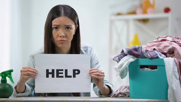 Upset Woman Showing Help Word on Cardboard, Laundry Basket With Clothes on Table