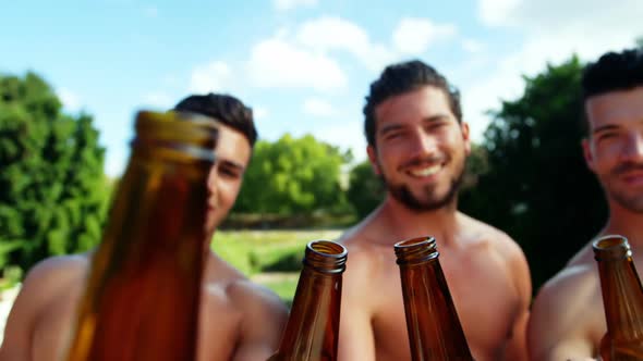 Group of male friends toasting beer bottles at poolside