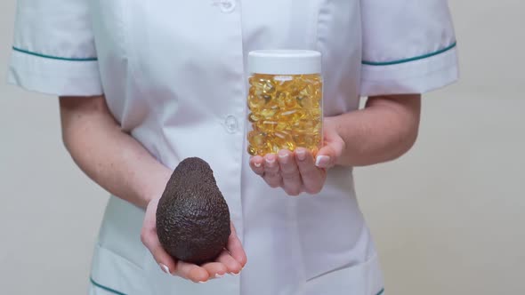 Nutritionist Doctor Holding Organic Avocado Fruit and Jar of Medicine or Vitamin or Omega 3 Capsules