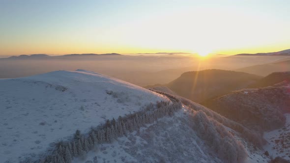 Aerial View of Sunset Sunrays Shining on Winding Mountain Road and Snow Covered Peaks